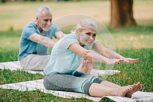 Focus of smiling, mature man and woman sitting in stretching poses while practicing yoga in park