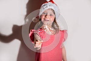 Focus on sparklers. merry girl in a red cap celebrates Christmas in blur on a white background