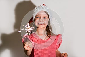 Focus on sparklers. smiling girl in a red cap celebrates Christmas in blur on a white background