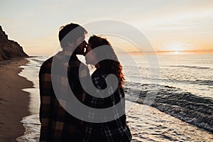 Focus on the sunrise and sea, young couple, woman and man holding by hands together and walking along the sea coast at