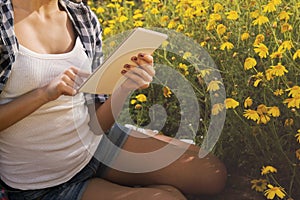 Focus on tablet into the hands of a beautiful girl on grass