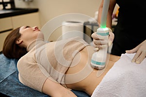 Focus on a touch ultrasonic transducer moving over contact gel lubricated belly of young woman receiving body shaping cavitation