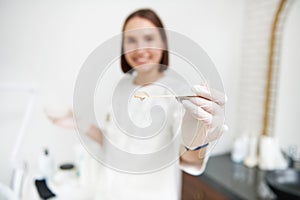 Focus on transparent gel with anaesthetic on the wooden spatula in the hand of blurry young doctor in the background