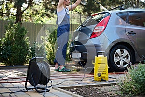 Focus on water high pressure cleaner against blurred man directing spray wand with water jet on his car while washing it