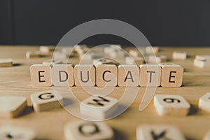 Focus of word educate made of cubes surrounded by blocks with letters on wooden surface isolated on black