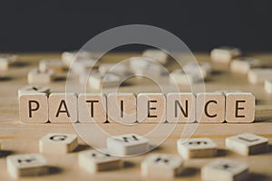 Focus of word patience made of cubes surrounded by blocks with letters on wooden surface isolated on black