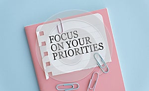 FOCUS ON YOUR PRIORITIES, text on white paper on blue table