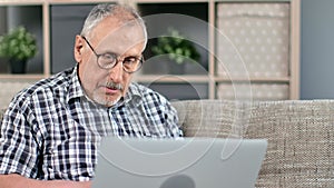 Focused 70s grandfather chatting surfing internet use laptop pc on couch medical service application