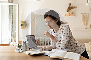 Focused adult female student doing homework, reading books at laptop