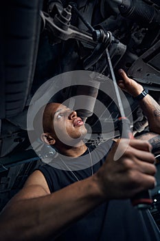 Focused African American car-mechanic checking car axle and lever integrity