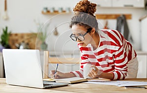 Focused african american female freelancer looking at laptop taking notes during remote team meeting