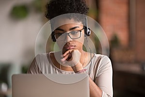 Focused african american girl student wearing headphones looking at laptop