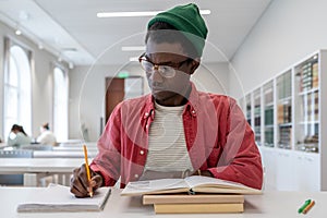 Focused african american guy college student sitting at desk with textbooks, studying in library