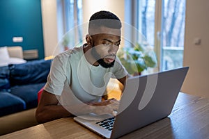 Focused African American guy freelancer working on laptop at home office, feeling overwhelmed