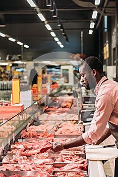 focused african american male butcher in apron taking steak of raw meat