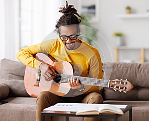 Focused african american male musician with classic acoustic guitar reading sheet music on paper