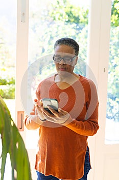 Focused african american senior woman using smartphone in sunny living room, copy space