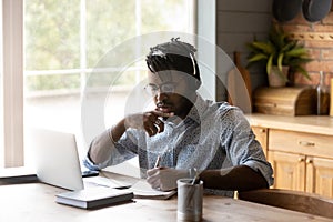 Focused African American student guy in headphones watching learning webinar