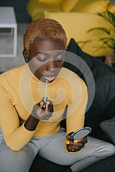 Focused african american woman applying lip gloss and looking photo