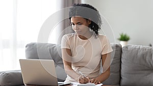 Focused African American woman using laptop, making notes