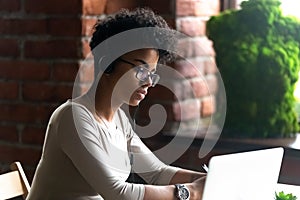 Focused African American woman wearing headphones using laptop