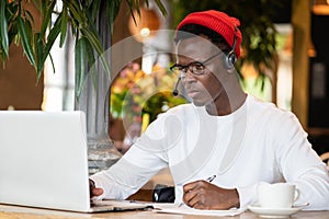 Concentration black hipster male in headphones, eyewear studing or working remotely on computer