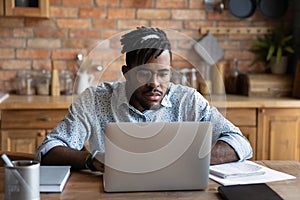 Focused African student guy studying from home, watching learning webinar