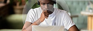 Focused African student wear headphones studying using laptop horizontal photo