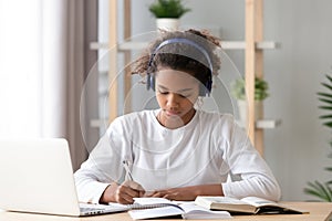 Focused african african teen girl wearing headphones writing notes studying photo