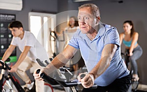 Aged man doing cardio workout on exercise bike in gym