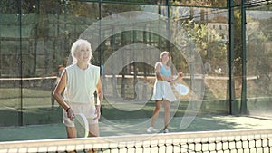 Focused aged woman playing friendly paddleball match on outdoor summer court. Senior people sports concept