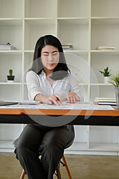 Focused Asian businesswoman working on the financial report spreadsheet at her desk