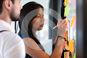 Focused asian businesswoman writing on sticky notes on glass