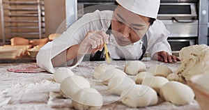 Focused asian female baker working in bakery kitchen, cutting dough for rolls in slow motion