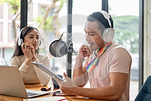 A focused Asian gay man radio host is talking and interviewing his guest in the studio