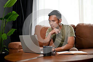 Focused Asian man looking at his laptop screen, planning a plan for his business project