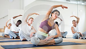 Focused asian woman practicing Hatha yoga postures with group