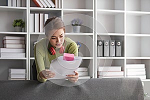 Focused asian woman stands in her living room checking her bills and planning her household expenses.