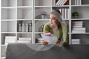 Focused asian woman stands in her living room checking her bills and planning her household expenses.