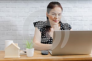 Focused Asian woman using laptop at home, looking at screen, chatting, reading or writing email