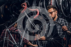 Focused attractive man in glasses is chainging wheel for bicycle at busy workshop