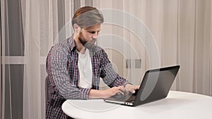 Focused Bearded businessman working on laptop computer at home office.
