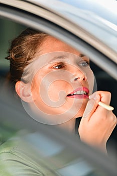 A focused beautiful woman using a lip profiler on her lips inside a car. Makeup and beauty concept