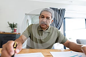 Focused biracial senior man analyzing bills on wooden table while sitting at home