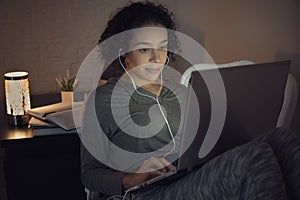 Focused black female student with curly short hair taking an online classes on laptop and looking at screen. Indoors at home