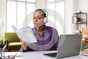 Focused black female student reviewing notes while attending an online course