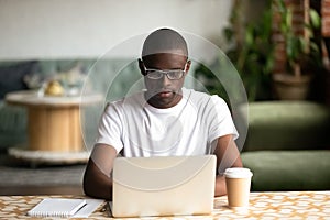 Focused black man studying on laptop drinking coffee