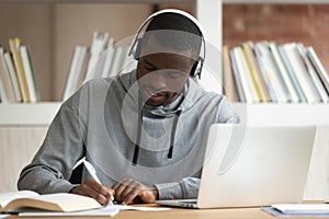 Focused black student wearing bluetooth earphones, busy with study,