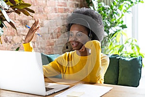 Focused black woman employee wear headphones, talking on zoom app with clients on laptop, consulting customer, giving online
