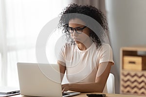 Focused black woman in glasses busy working at laptop